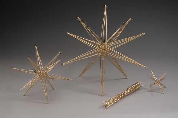 A beautifully crafted 6 Axis Star made of silicon bronze, designed by John Kostick. The image showcases three distinct star figures of varying sizes, emphasizing their intricate design and shine. The pieces are arranged on a neutral background, highlighting their geometric shapes and polished finish. This artistic meditation toy or decorative piece adds elegance to any space.
