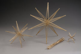 The Tetraxis Star4 in Bronze by John Kostick features a stunning design with multiple star-shaped structures formed from slender metallic rods, showcasing artistic craftsmanship. The product includes varying sizes of stars arranged aesthetically, perfect for decorative purposes or as a unique art piece.