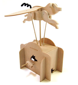 A whimsical wooden DIY kit featuring a flying pig with outstretched wings, supported by strings. The pig is attached to a base resembling a box with a winding mechanism, perfect for crafting and play. The kit showcases intricate wooden details and provides an engaging building experience.