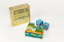 A jigsaw puzzle titled 'Boston City Squares' by Boston Folk Art. The box features the words 'Six Original Images of Boston' with colorful graphics representing iconic Boston landmarks. The puzzle pieces showcase artwork of the Public Garden, Swan Boats, and other famous Boston sites.