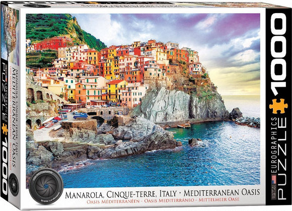 Eurographics jigsaw puzzle featuring a picturesque scene of Manarola in Cinque Terre, Italy. The image showcases colorful coastal houses perched on cliffs overlooking the clear blue Mediterranean sea and rocky shores, perfect for puzzle enthusiasts.