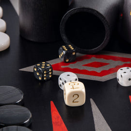 A close-up view of a 19-inch black oak and silver Backgammon set by Manopoulous, featuring black and white game pieces, intricate red and grey designs on the board, and dice arranged on the playing surface.