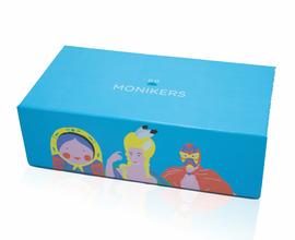 A bright blue game box titled 'Monikers' by CMYK, featuring whimsical illustrations of three characters: a woman with a yellow headscarf, a blonde woman in a stylized gown, and a masked superhero. The design is colorful and playful, suggesting a fun party game experience.