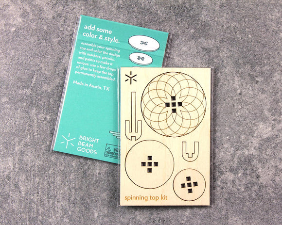 Spinning Tops Dahlia DIY kit by Bright Beam Goods. The kit includes pre-cut wooden pieces featuring engaging designs for assembly and coloring. It is packaged with a colorful instruction card that encourages creativity with markers and paints. Made in Austin, TX.
