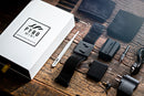 The Pyro Mini V4 Bundle by ELusionist laid out on a rustic wooden surface. The image features a white box with the Pyro Mini logo prominently displayed, along with various components including a wrist strap, battery pack, wires, an instruction tool, and two types of adapters.