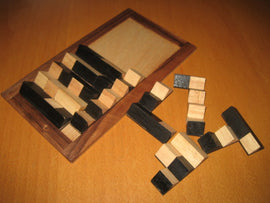 PentoTwo by Dor Tietz is a mechanical puzzle featuring a wooden board with various black and natural wooden blocks. The blocks are arranged on the board and scattered beside it, designed to challenge problem-solving skills and spatial reasoning. The puzzle's elegant design and tactile nature make it an engaging activity for all ages.