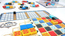 An image showcasing the game Azul by Plan B Games. The game features colorful tiles in red, blue, yellow, and black on player boards, with a central scoring area and multiple tile supply boards. Players can be seen arranging their tiles strategically in an engaging manner.