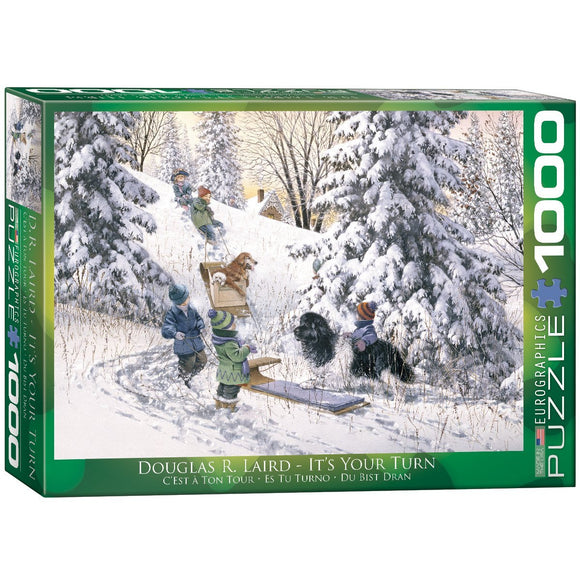 The box of the jigsaw puzzle titled 'It's Your Turn' by Eurographics, featuring an illustration by Douglas R. Laird. The scene shows children and dogs playing in a snowy landscape, with sleds and a backdrop of evergreen trees and a distant house. The puzzle contains 1000 pieces, ideal for family fun and relaxation.