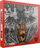 The box cover for the game 'Squirrel or Die' by Atlas Games, featuring a cartoonish squirrel smiling while holding an acorn. Above it, a menacing owl looms with outstretched wings, set against a monochrome background that contrasts with the bright red border of the box. The title is prominently displayed on the side of the box.