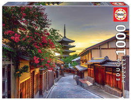 Educa jigsaw puzzle featuring a scenic view of YASAKA PAGODA in Kyoto, Japan. The image captures traditional Japanese architecture, flowering trees, and a tranquil street at sunset, offering a serene and immersive experience for puzzle enthusiasts.