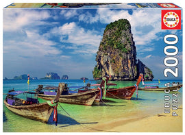 Educa 2000-piece jigsaw puzzle featuring a picturesque scene from Krabi, Thailand. The image shows traditional boats anchored in clear turquoise waters with a lush green rock formation in the background under a partly cloudy sky.