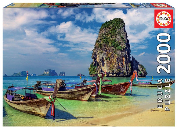 Educa 2000-piece jigsaw puzzle featuring a picturesque scene from Krabi, Thailand. The image shows traditional boats anchored in clear turquoise waters with a lush green rock formation in the background under a partly cloudy sky.