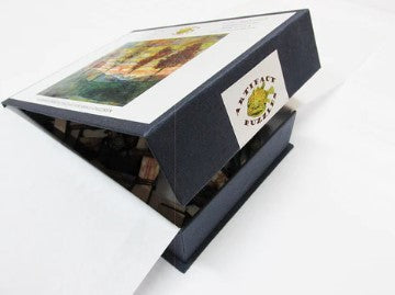 The Artifact Wooden Puzzles jigsaw puzzle box featuring 'Four Trees' by Egon Schiele. The box is partially open, revealing a glimpse of the pieces inside. A colorful artwork of four trees is displayed on the lid.