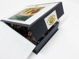 The Artifact Wooden Puzzles jigsaw puzzle box featuring 'Four Trees' by Egon Schiele. The box is partially open, revealing a glimpse of the pieces inside. A colorful artwork of four trees is displayed on the lid.