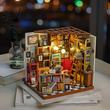 Sam's Study Model Kit by Robotime, a detailed DIY miniature scene featuring a cozy study with bookshelves filled with colorful books, a red armchair, a wooden ladder, and warm lighting, perfect for creative building and design enthusiasts.