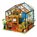 Cathy's Flower House Model Kit by Robotime, featuring a detailed greenhouse with vibrant plants, a blue door, and rustic decorations. Perfect for DIY enthusiasts, this kit includes miniature gardening tools and accessories, creating a charming floral display.