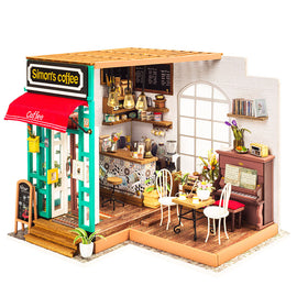 A detailed model kit of Simon's Coffee, showcasing a quaint coffee shop exterior with a red awning and bright teal frame. The interior features a cozy coffee bar, wooden flooring, a vintage piano, various furniture pieces including tables and chairs, decorative plants, and wall-mounted shelves filled with books. Various coffee-making equipment and decor items enhance the inviting atmosphere of this miniature café.