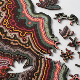 Close-up view of the Orbicular Geode Puzzle by Nervous System, showcasing intricate jigsaw puzzle pieces with vibrant colors and swirling patterns resembling geological formations. Several pieces are laid out, revealing the puzzle's artistic design and unique shapes that enhance the assembling experience.