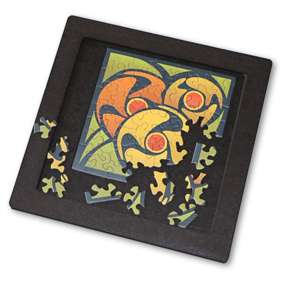 Curiosi Puzzle Tray Medium, a jigsaw puzzle featuring an artistic design with vibrant colors. The tray displays an incomplete puzzle showing circular shapes in orange, yellow, and green, with some pieces scattered around the edges, set against a black background.