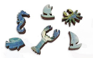 A collection of intricately cut wooden jigsaw puzzle pieces featuring artwork inspired by Van Gogh's 'Sea at Saint-Maries'. The pieces include a seahorse, a lobster, a crab, and abstract waves, showcasing vibrant blues and greens.