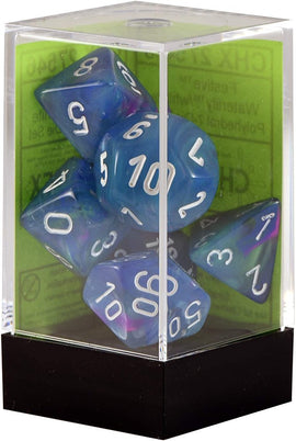 A display case containing a set of Festive Waterlily polyhedral dice by Chessex. The dice are a blend of blue and purple colors with white numbers, showcasing a variety of shapes including d4, d6, d8, d10, d12, and d20. The background of the display is green, indicating that these gaming dice are perfect for tabletop gaming enthusiasts.
