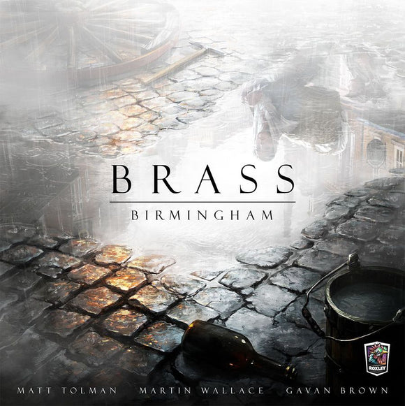 The game 'Brass: Birmingham' by Roxley Games features a beautifully illustrated cover depicting a cobblestone street scene with reflections in the wet stones. A rustic bucket and a tipped-over bottle are also visible, evoking a historical setting.