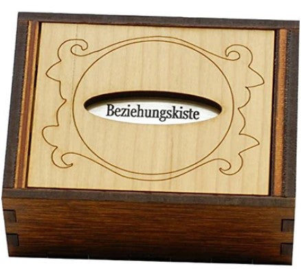 Beziehungskiste by Jean-Claude Constantin is a beautifully crafted mechanical puzzle box made of wood. It features intricate designs on the surface and a central slot labeled 'Beziehungskiste', suggesting a unique function or interactive element, perfect for puzzle enthusiasts and gift-givers alike.