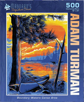 A colorful jigsaw puzzle featuring the Boundary Waters Canoe Area, designed by Adam Turman. The image showcases a serene scene with a vibrant sunset, a canoe along the water, and silhouetted trees, captured in a 500-piece format that measures 18x24 inches.