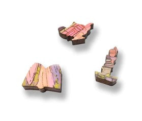 Three intricately designed wooden jigsaw puzzle pieces showcasing vibrant colors and unique shapes, including a book and a whimsical design, highlighting the artistic elements of 'The Bookkeeper' jigsaw puzzle by Nicole Gustafsson, made by Artifact Wooden Puzzles.
