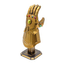 A detailed metal model of the Infinity Gauntlet from the Avengers, featuring intricate designs and colorful gem-like embellishments. The gauntlet is gold-colored and stands on a decorative base, showcasing the craftsmanship of the DIY kit by Fascinations.