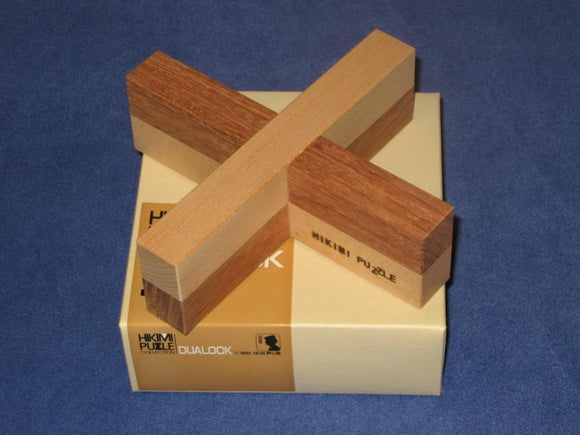 The Dualock Hikimi puzzle features a unique cross design made of light and dark wood, resting on its branded box. This mechanical puzzle challenges your problem-solving skills with its intricate assembly.
