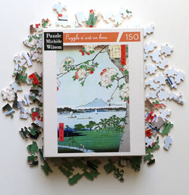 Apple Blossoms jigsaw puzzle by Wilson Jeux featuring a vibrant artwork of blooming apple trees against a scenic landscape. The puzzle is surrounded by its colorful pieces, showcasing artistic design and intricate details.