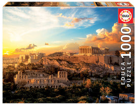 A box displaying the ACROPOLIS OF ATHENS jigsaw puzzle by Educa. The image showcases the iconic Acropolis under a vibrant sunset sky, surrounded by lush greenery and historical ruins. The puzzle contains 1000 pieces, offering a beautiful and engaging way to explore ancient Greek architecture and scenery.