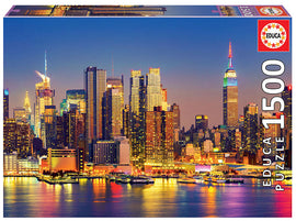 MANHATTAN AT NIGHT 1500PC jigsaw puzzle by Educa, featuring a stunning skyline view of New York City illuminated at night, showcasing iconic buildings like the Empire State Building. The vibrant colors of the city lights reflect off the water, creating a captivating scene for puzzle enthusiasts.