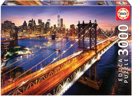 Educa jigsaw puzzle 'Manhattan at Sunset' featuring a stunning view of the Manhattan skyline illuminated by sunset. The vibrant colors of the city lights reflect on the water beneath the iconic bridge, making it a captivating 3000-piece challenge for puzzle enthusiasts.