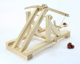 DIY Roman Catapult kit by Pathfinders. The wooden catapult features a detailed design with levers and a launch mechanism, accompanied by small clay projectiles for play.
