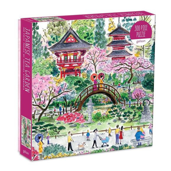 A beautifully illustrated box for the Japanese Tea Garden jigsaw puzzle by Galison. The artwork depicts a serene garden scene featuring colorful cherry blossoms, traditional Japanese architecture, a charming bridge, and people enjoying the scenery. It includes vibrant colors and intricate details that invite puzzle enthusiasts to engage in this 300-piece challenge.