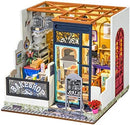 A detailed miniature DIY kit of Nancy's Bake Shop, featuring a quaint bakeshop with a charming front display, decorative signage, and a cozy interior filled with baking tools, pastries, and floral arrangements. The model showcases vibrant colors and intricate designs, making it perfect for creative crafting enthusiasts.