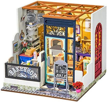A detailed miniature DIY kit of Nancy's Bake Shop, featuring a quaint bakeshop with a charming front display, decorative signage, and a cozy interior filled with baking tools, pastries, and floral arrangements. The model showcases vibrant colors and intricate designs, making it perfect for creative crafting enthusiasts.