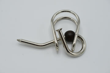 A U-Nagel mechanical puzzle by Jean-Claude Constantin, featuring intricate metal loops and a wooden bead. The design showcases a unique twisting mechanism aimed at providing mental stimulation and challenging users to find solutions. Ideal for puzzle enthusiasts and those looking for a brain teaser.