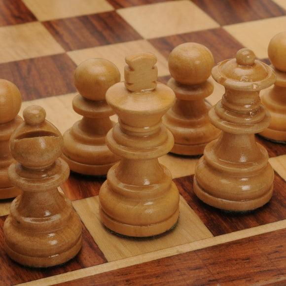 Close-up view of intricately designed wooden chess pieces on a polished chessboard. The pieces are magnetized for ease of use, showcasing the king, queen, and pawns in a classic setup.