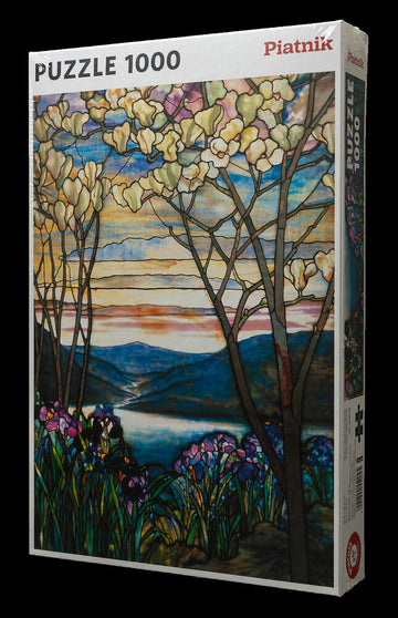 A 1000-piece jigsaw puzzle titled 'Tiffany Magnolia & Irises' by Piatnick displayed in its box. The artwork features vibrant magnolia flowers and irises in a serene landscape, showcasing rich colors and intricate designs. The scene includes trees with blossoms, a flowing river, and distant mountains under a colorful sky at dusk, making it a beautiful and challenging puzzle for enthusiasts.