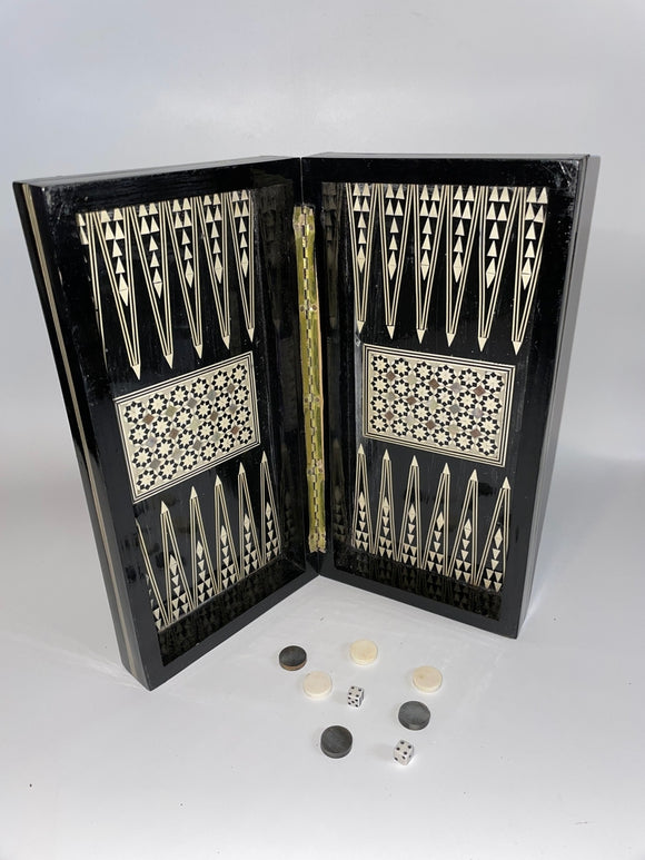 A beautifully crafted 12-inch Backgammon board featuring mother-of-pearl inlays. The board is opened and displays intricate geometric patterns. Several gaming pieces and dice are positioned around the board on a smooth, neutral background.