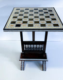 Elegant chess table featuring a mother of pearl inlaid design. The table has a classic chessboard layout with alternating black and light squares, surrounded by intricate detailing. The sturdy base offers a traditional aesthetic suitable for any gaming room or living space.