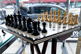 A beautifully crafted chess table featuring a mother of pearl inlay and intricate designs. The board displays black and beige chess pieces ready for a game, showcasing a vibrant and elegant design.