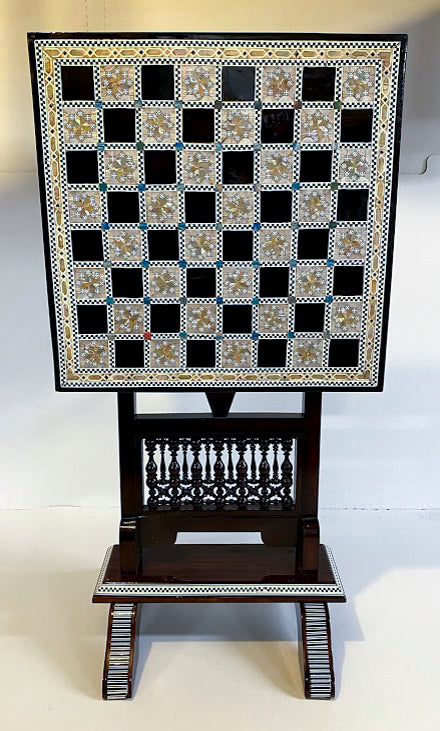 Beautiful chess table featuring a mother of pearl inlaid board with intricate designs. The table has a standing frame with detailed carvings, offering an elegant way to play chess. Perfect as a decorative piece and functional gaming table.