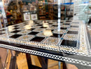 Elegant chess table featuring a mother of pearl inlay. The surface showcases intricate patterns with alternating black and white squares, bordered by decorative motifs, enhancing its aesthetic appeal. Perfect for stylish game nights.