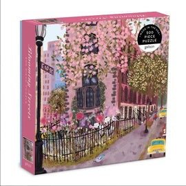 The Blooming Streets jigsaw puzzle by Galison showcases a charming street scene adorned with blossoming trees, vintage buildings, and a welcoming sidewalk lined with blooming flowers. The packaging features a whimsical illustration that invites puzzle enthusiasts to immerse themselves in a picturesque urban landscape. This 500-piece puzzle brings together art and the joy of puzzling, offering an entertaining activity for all ages.