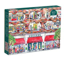 A colorful jigsaw puzzle box titled 'A Day at the Bookstore' by Galison, featuring an illustration of a bustling bookstore with various sections such as children's books, poetry, and used books. The design includes characters engaged in activities like reading and shopping, along with trees and bicycles outside.