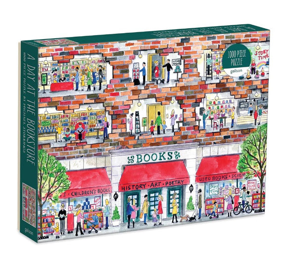 A colorful jigsaw puzzle box titled 'A Day at the Bookstore' by Galison, featuring an illustration of a bustling bookstore with various sections such as children's books, poetry, and used books. The design includes characters engaged in activities like reading and shopping, along with trees and bicycles outside.